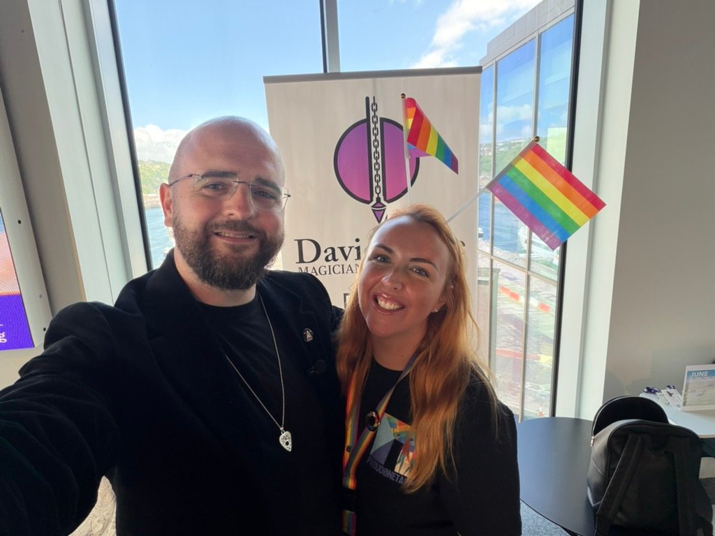 David Peace with an attendee at a Pride month event after a public speaking talk, with rainbow flags behind them