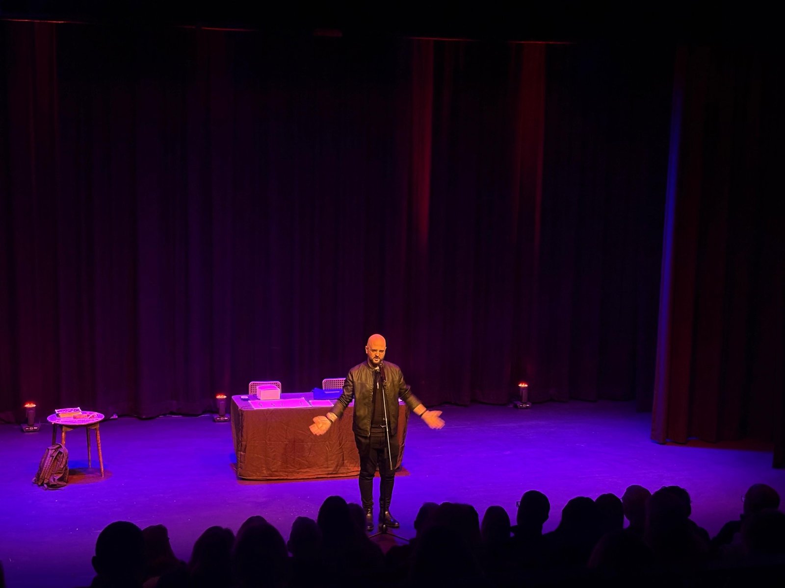 David Peace on stage with his arms open, addressing an audience